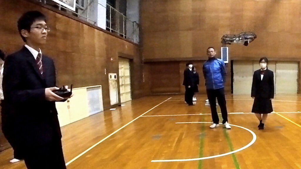 高校体育館にて、高校生がドローンの操作を体験している様子